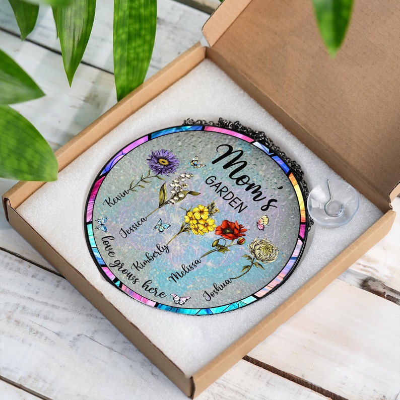 May include: A round glass suncatcher with a blue, green, and purple stained glass design. The suncatcher features a floral design with butterflies and the text "Mom's Garden". The names Kevin, Jessica, Kimberly, Melissa, and Joshua are written around the edge of the suncatcher.