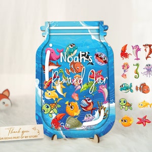 May include: A blue wooden reward jar with a sea-themed design. The jar has a slot for inserting tokens and features the text "Noah's Reward Jar". The jar is surrounded by colorful sea creatures, including fish, a turtle, a starfish, and a whale.