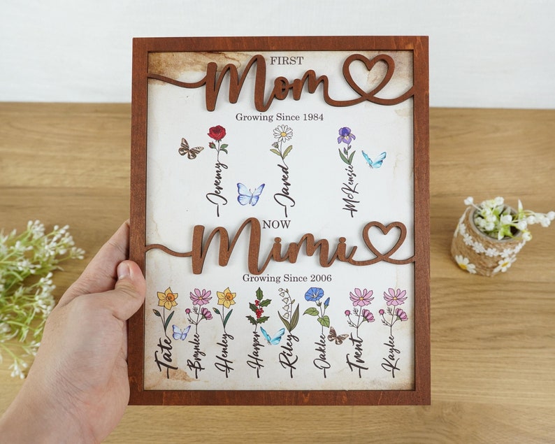 May include: A wooden framed sign with the words "First Mom Growing Since 1984" and "Now Mimi Growing Since 2006" with a heart symbol after each. The sign has a floral design with names of children written on each flower.