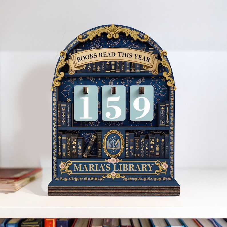 May include: A navy blue wooden bookshelf-shaped book tracker with the text "BOOKS READ THIS YEAR" and "MARIA'S LIBRARY". The tracker displays the number 159 on three light blue panels. The design includes gold accents and illustrations of books.