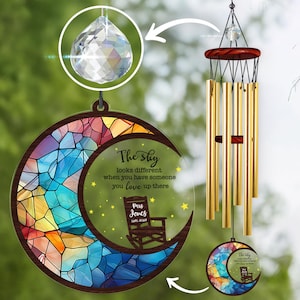May include: A wind chime with a stained-glass moon design, featuring a quote and a rocking chair illustration. The chime has gold-colored tubes and a crystal pendant. The text reads "The sky looks different when you have someone you love up there."