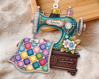 May include: A teal sewing machine Christmas ornament with the name "Amelia" on it. The ornament features a colorful quilt and floral accents. The sewing machine is detailed with silver and gold accents, and a pink spool of thread.