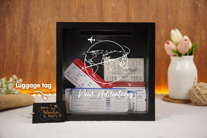 May include: Black shadow box with a white globe and airplane design. The box contains several airline boarding passes and a save the date card that reads "KATIE & CHRIS". A luggage tag with the text "And so... the Adventure Begins" is in the lower left corner of the image.