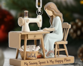 May include: A wooden Christmas ornament depicting a person sewing at a sewing machine. The ornament features a light-colored sewing machine, a wooden table, and a person in a dress. The base of the ornament reads "My Sewing Space Is My Happy Place."