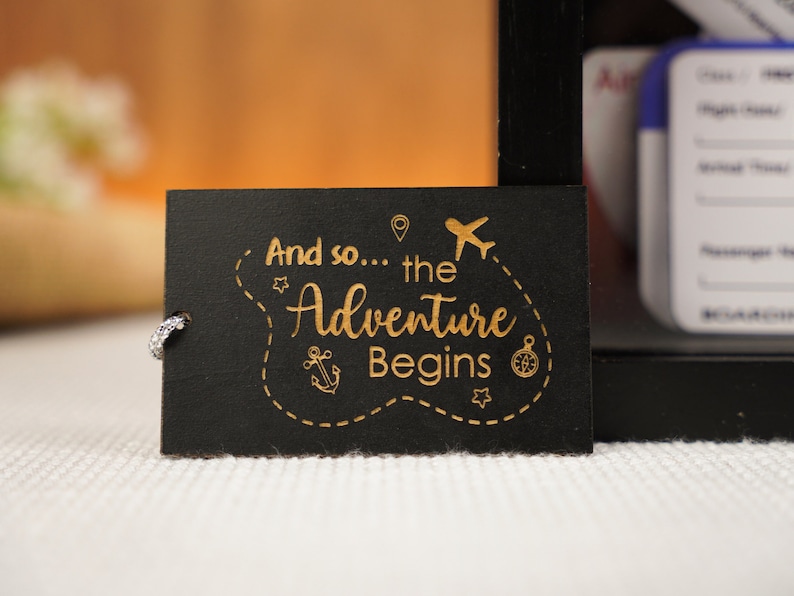 May include: Black wooden sign with gold lettering that reads "And so... the Adventure Begins". The sign features a compass, anchor, airplane, and a star.