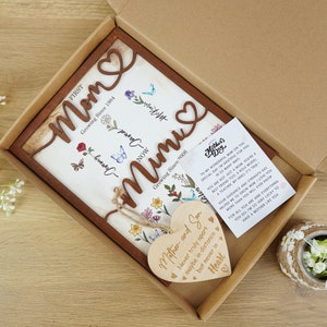May include: A wooden sign with the words "Mom" and "Mimi" in a decorative font. The sign is decorated with flowers and butterflies. The sign is in a brown wooden frame and comes with a small wooden heart with the text "Mother and Son Never truly apart maybe in distance but never in heart".