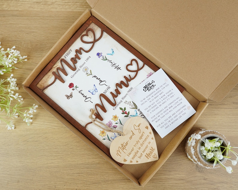 May include: A wooden sign with the words "Mom" and "Mimi" in a decorative font. The sign is decorated with flowers and butterflies. The sign is in a brown wooden frame and comes with a small wooden heart with the text "Mother and Son Never truly apart maybe in distance but never in heart".