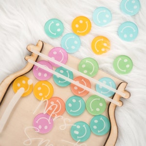 May include: A wooden jar with a clear plastic lid and two clear plastic straws. The jar is filled with colorful smiley face tokens. The jar is labeled "Mrs. Smith".