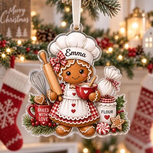 May include: A clear acrylic Christmas ornament featuring a gingerbread character wearing a chef hat with the name Emma, a red and white gingham apron, and holding a rolling pin and red bowl. Includes a red mug labeled Baked With Love.