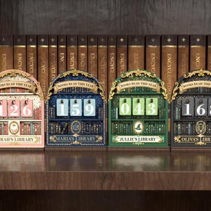 May include: Four decorative wooden book counters in pink, blue, green, and black, each with a different number displayed. The counters have a library theme, with the words "Books Read This Year" above the numbers and the names "Sarah's Library", "Maria's Library", "Jullie's Library", and "Oliva's Library" below.