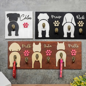 May include: Wooden dog butt shaped hooks with names and paw prints. The hooks are mounted on a brown wooden board. The names are Chloe, Mulk, Gita, Milly, Rick, and Mauso.