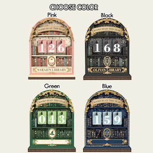 May include: A wooden bookshelf-shaped book counter in pink, black, green, and blue. Each counter displays a three-digit number, with the text "BOOKS READ THIS YEAR" above. The pink counter reads 126, the black reads 168, the green reads 043, and the blue reads 159.