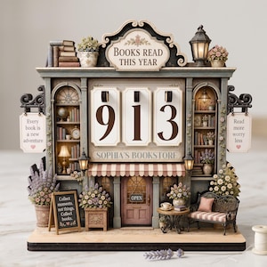 May include: A decorative tabletop display shaped like a bookstore with the text BOOKS READ THIS YEAR, SOPHIA'S BOOKSTORE, and signs reading Every book is a new adventure, Read more worry less, and Collect moments, not things, Collect books. It shows 913.