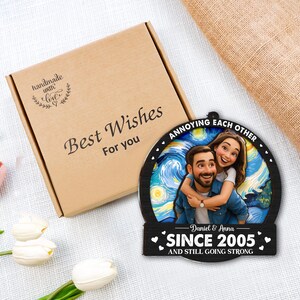 May include: A personalized wooden ornament featuring a couple embracing, set against a starry night backdrop. The ornament reads "Annoying each other since 2005 and still going strong." A brown gift box with "Best Wishes for you" is also in the image.