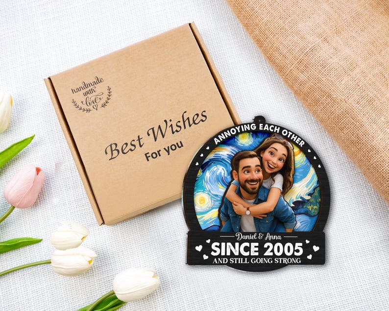 May include: A personalized wooden ornament featuring a couple embracing, set against a starry night backdrop. The ornament reads "Annoying each other since 2005 and still going strong." A brown gift box with "Best Wishes for you" is also in the image.