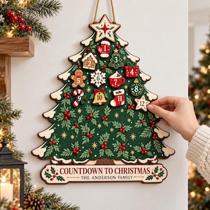 May include: A wall-hanging wooden Christmas tree advent calendar featuring twelve numbered ornaments. The green tree is decorated with red berries and gold stars, with a base plate reading COUNTDOWN TO CHRISTMAS THE ANDERSON FAMILY.
