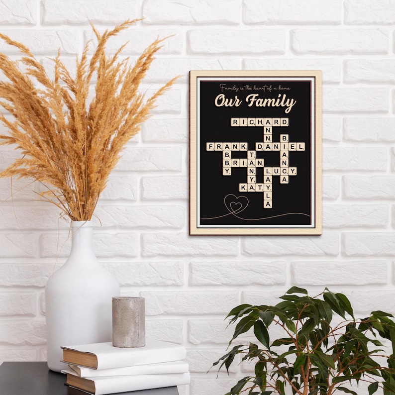 May include: Black and white sign with the words "Our Family" in gold lettering. The sign features a crossword puzzle made of wooden tiles with the names "Richard", "Frank", "Daniel", "Brian", "Tanya", "Lucy", and "Katy" spelled out.