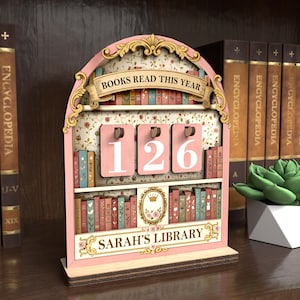 May include: A pink wooden bookshelf-shaped book counter with the text "BOOKS READ THIS YEAR" and "SARAH'S LIBRARY". The counter displays the number 126. The design includes floral patterns and decorative elements.