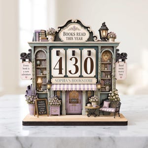 May include: A decorative tabletop bookstore display featuring the text BOOKS READ THIS YEAR and SOPHIA'S BOOKSTORE. The structure includes a central counter with the number 430, a purple door, bookshelves, floral arrangements, and two hanging signs.