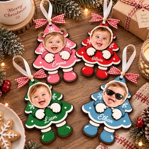 May include: Four wooden Christmas tree ornaments featuring personalized photos of children's faces. Each ornament is shaped like a tree with a white ribbon, a red and white checkered bow, and a name printed in white: Emma, Olivia, Liam, and Ethan.