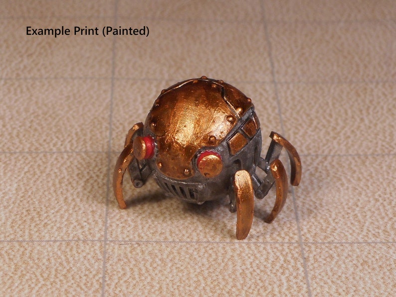 May include: A small, metallic, gold-painted spider-like robot with red eyes. The robot has a round body with a segmented design and six legs.
