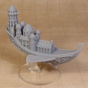 May include: A light gray 3D printed miniature of a fantasy boat carrying a multi-towered building structure. The vessel features curved sides with ornate scrollwork, fin-like side protrusions, and a pointed prow, all mounted on a clear circular base.