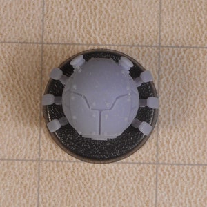 May include: A gray, plastic, spider-like robot with six legs and a round body. The robot is sitting on a black base.