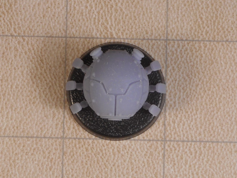May include: A gray, plastic, spider-like robot with six legs and a round body. The robot is sitting on a black base.