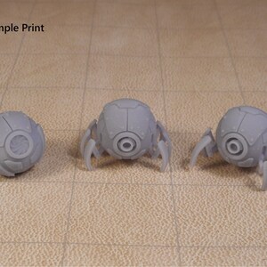 May include: Three 3D printed gray robots with round bodies and six legs each. The robots have a circular design on the front of their bodies.