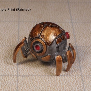 May include: A small, metallic, steampunk-style robot with a spherical body and six spindly legs. The body is painted in a copper color with silver accents and has a red eye. The legs are painted in a gold color.