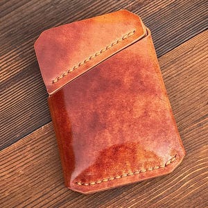 May include: A handcrafted, rectangular leather wallet with a marbled, reddish-brown finish. The wallet features a stitched border and a flap closure. The text at the bottom reads, "Each marbled Shell Cordovan pattern will be unique."