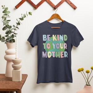 May include: A navy blue t-shirt with the text "Be Kind To Your Mother" in rainbow colors with a cartoon earth graphic.