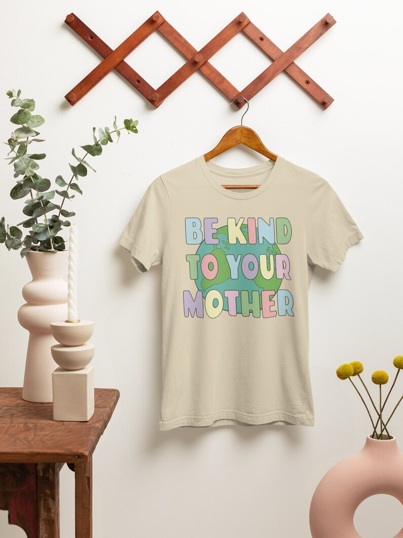 May include: Beige t-shirt with a colorful graphic of the Earth and the text "Be Kind To Your Mother".