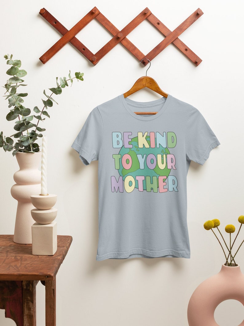 May include: A light blue t-shirt with the text "BE KIND TO YOUR MOTHER" in rainbow colors with a green, blue, and brown earth graphic in the middle of the text.