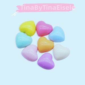 以下が含まれることがあります： 黄色、ピンク、青、オレンジ、ラベンダー、白など、さまざまなパステルカラーの9つのハート型のオブジェクトのコレクション。オブジェクトは、水色の背景に対して円形に配置されています。上部のテキストは「TinaByTinaEisele」です。