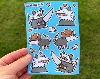 Könnte beinhalten: Ein Bogen mit blauen Aufklebern mit Cartoon-Opossums. Die Opossums sind mit Messern, Cowboyhüten und Herzen dargestellt. Der Text "i ❤️ trash" ist ebenfalls enthalten. Die Aufkleber stammen von "iMakeObjects".