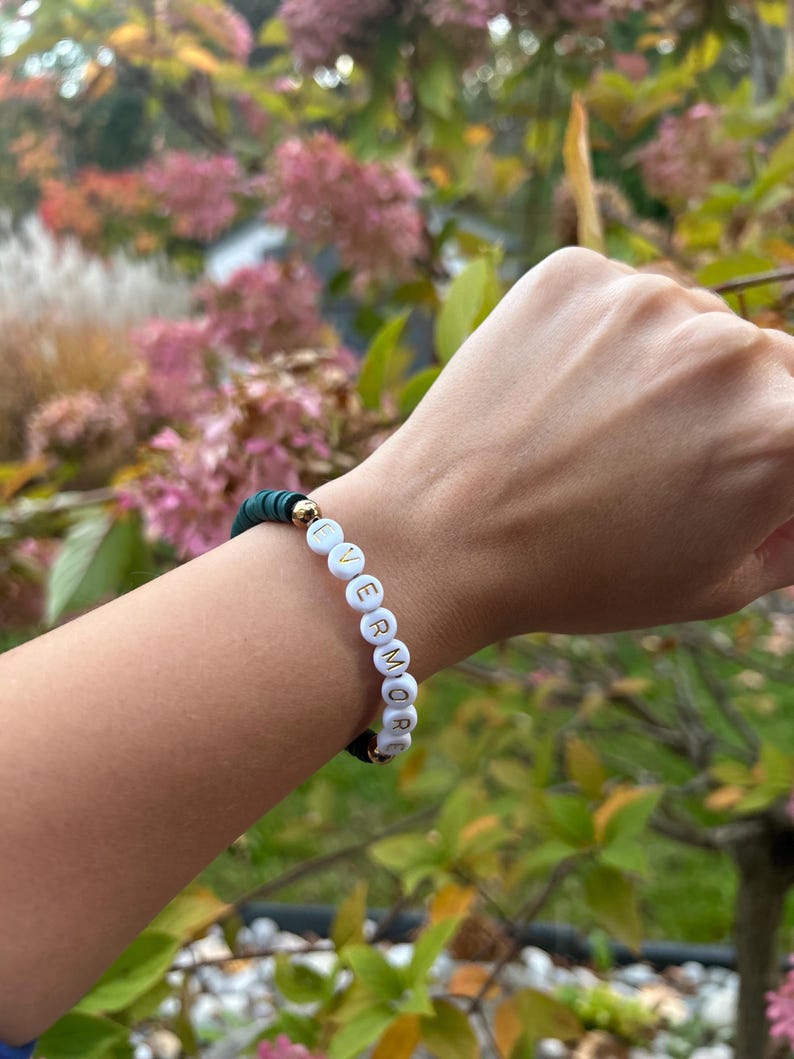 May include: A green beaded bracelet with white beads that spell out the word "evermore".