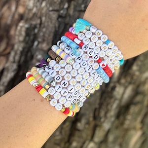 May include: A stack of colorful beaded bracelets with gold lettering spelling out words and phrases like "Fearless", "Love", "Midnight", and "Put A Ring On It".