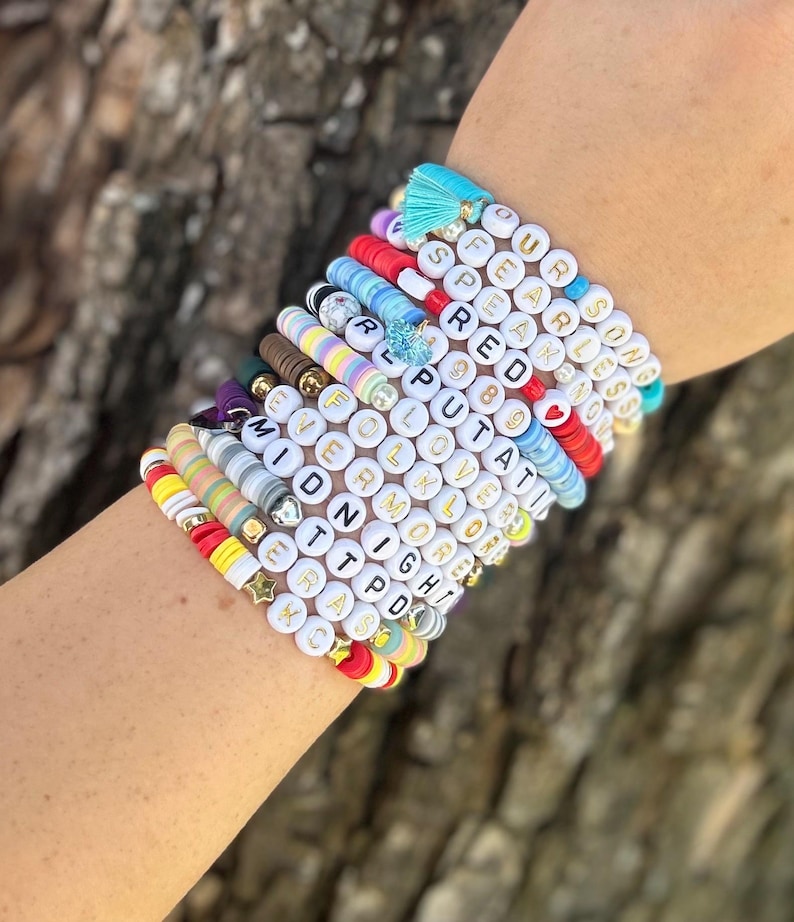 May include: A stack of colorful beaded bracelets with gold lettering spelling out words and phrases like "Fearless", "Love", "Midnight", and "Put A Ring On It".