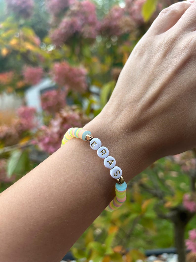 May include: A colorful beaded bracelet with the word "ERASE" spelled out in white letters on white beads. The bracelet is made with pastel blue, yellow, and pink beads.