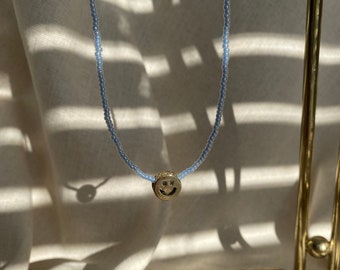Gold smiley face pendant on a strand of blue seed beads