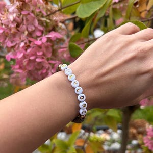 May include: A white beaded bracelet with gold lettering spelling out the word "FOLKLORE".