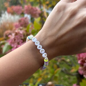 May include: A colorful beaded bracelet with white beads that spell out the word "LOVE" in gold letters.