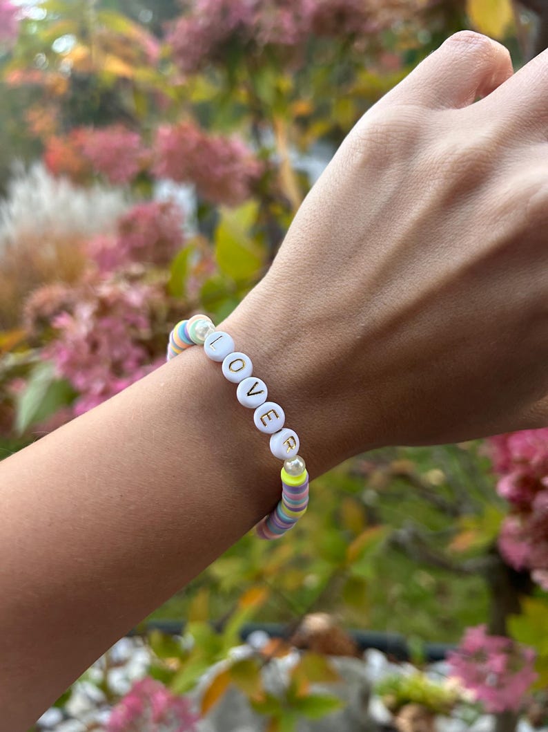 May include: A colorful beaded bracelet with white beads that spell out the word "LOVE" in gold letters.