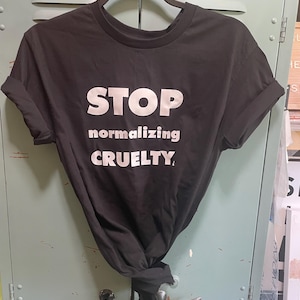 May include: Black t-shirt with white text that reads "STOP normalizing CRUELTY."