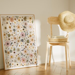 May include: A rectangular framed wall art print featuring a dense botanical pattern of pressed-style flowers in shades of pale pink, cream, muted yellow, and sage green, displayed next to a light-colored wooden chair with a straw hat and basket.