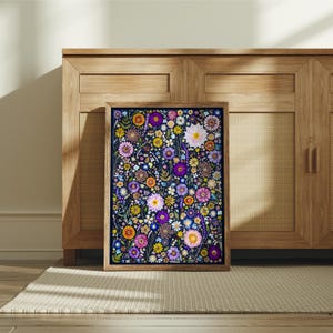 May include: A rectangular framed wall art print featuring a dense, colorful botanical illustration of various flowers including purple, pink, yellow, and white blossoms set against a dark navy blue background, encased in a light brown wooden frame.