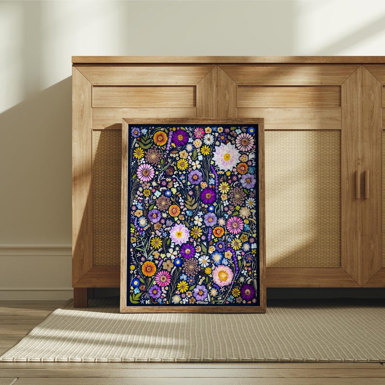 May include: A rectangular framed wall art print featuring a dense, colorful botanical illustration of various flowers including purple, pink, yellow, and white blossoms set against a dark navy blue background, encased in a light brown wooden frame.