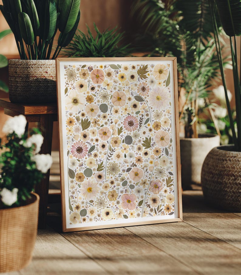 May include: A rectangular framed print featuring a dense collage of pressed flowers and foliage in shades of cream, pale yellow, soft pink, and muted green. The artwork is encased in a light-toned wooden frame with a clean, simple border design.
