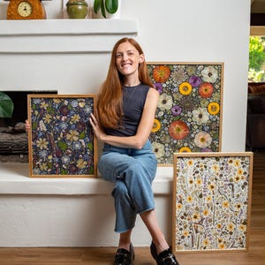 May include: Three rectangular framed art pieces featuring pressed flowers. One frame displays a dark blue background with yellow and white blossoms. Another shows vibrant orange, yellow, and purple flowers. The third features a light, botanical arrangement.